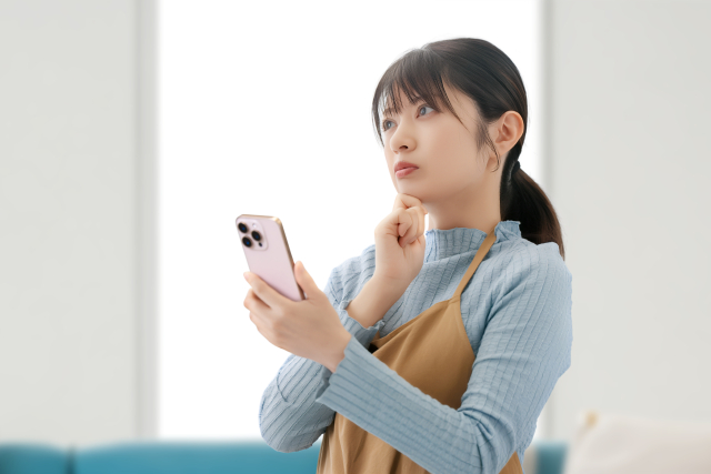 スマートフォンを手に、貯蓄について考える女性のイメージ