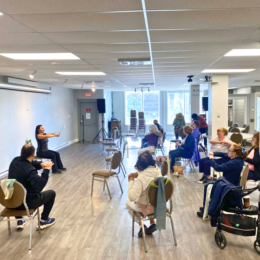 Older adults taking part in a seated exercise class led by an instructor at First Point