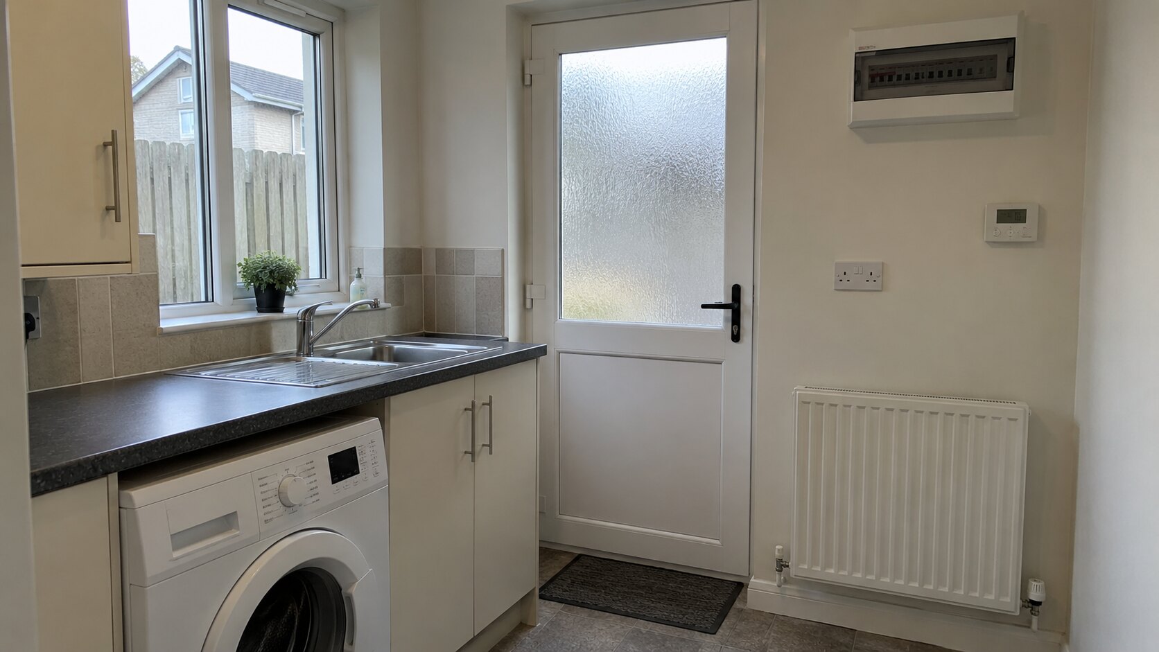 Utility room with a sink, washing machine, radiator, thermostat and consumer unit.