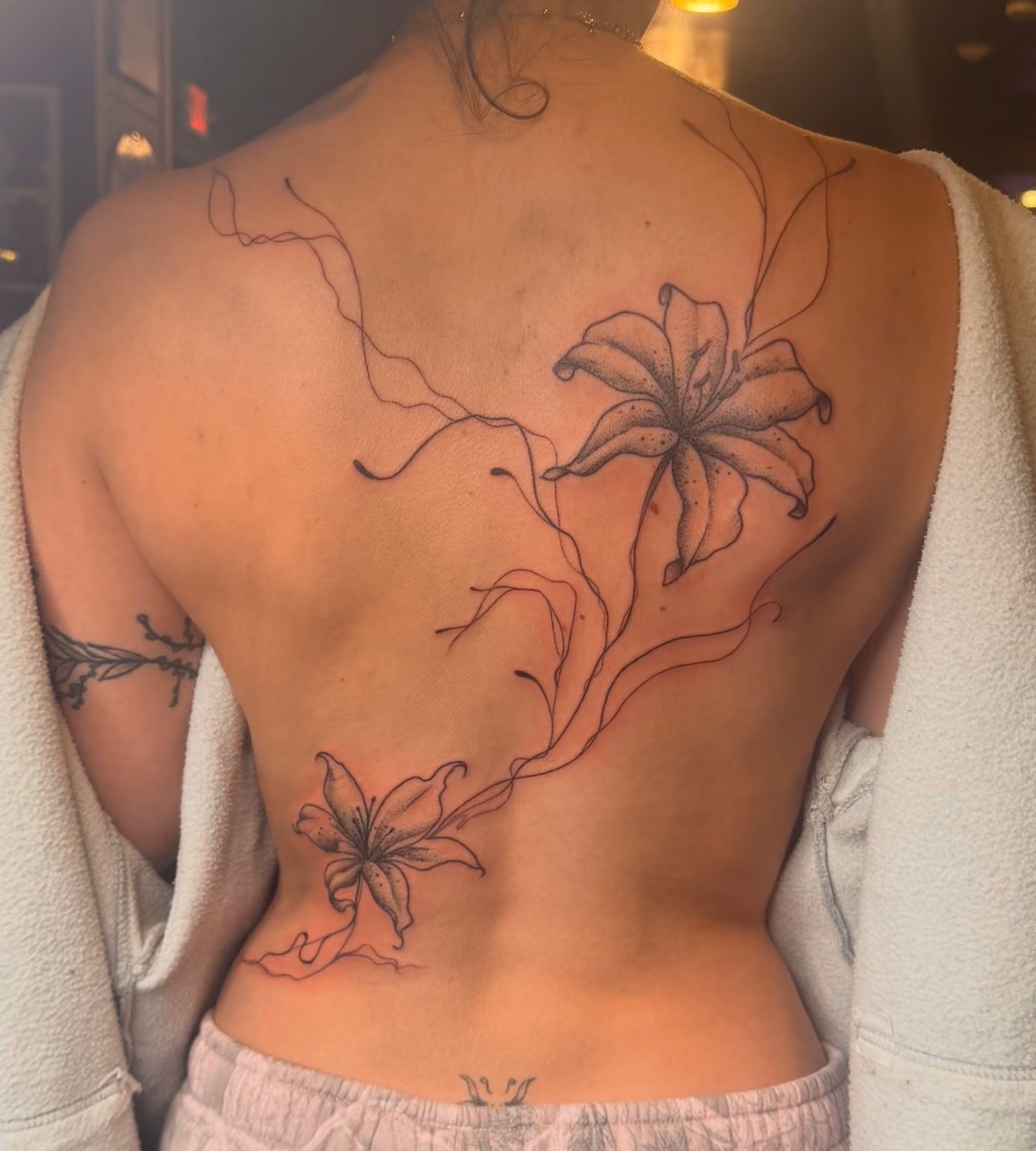Fine line lily back piece tattooed at Thorn & Dagger Ink