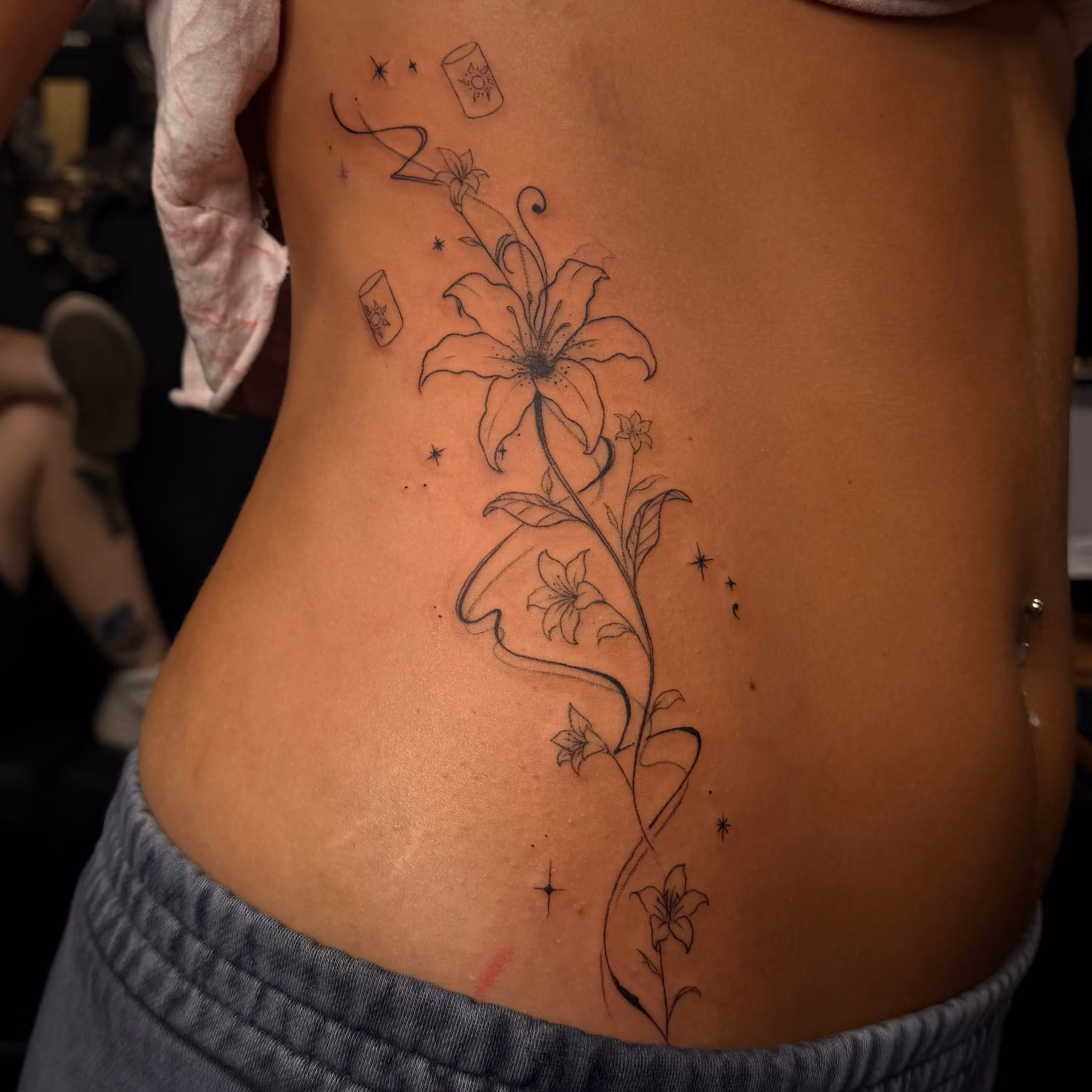 Fine line lily tattoo along the ribs