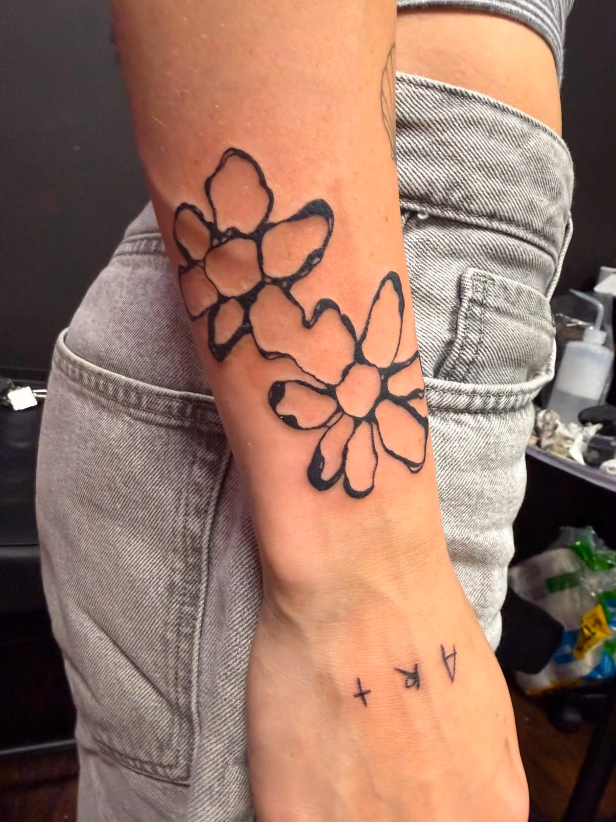Fine line wrist flowers tattoo at Thorn & Dagger Ink