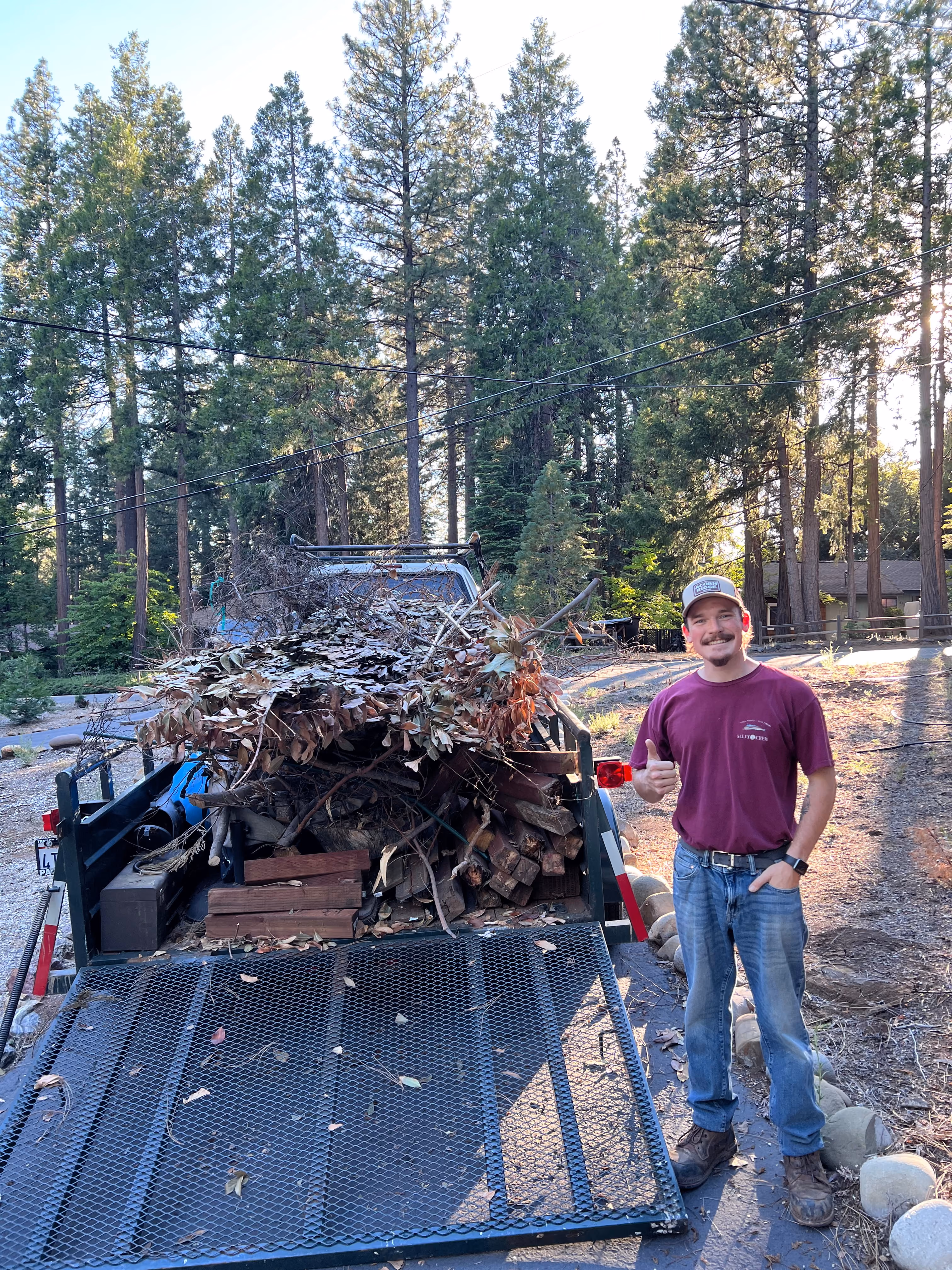 Aidan beside a trailer loaded with branches, leaves and scrap wood after a yard clearing job