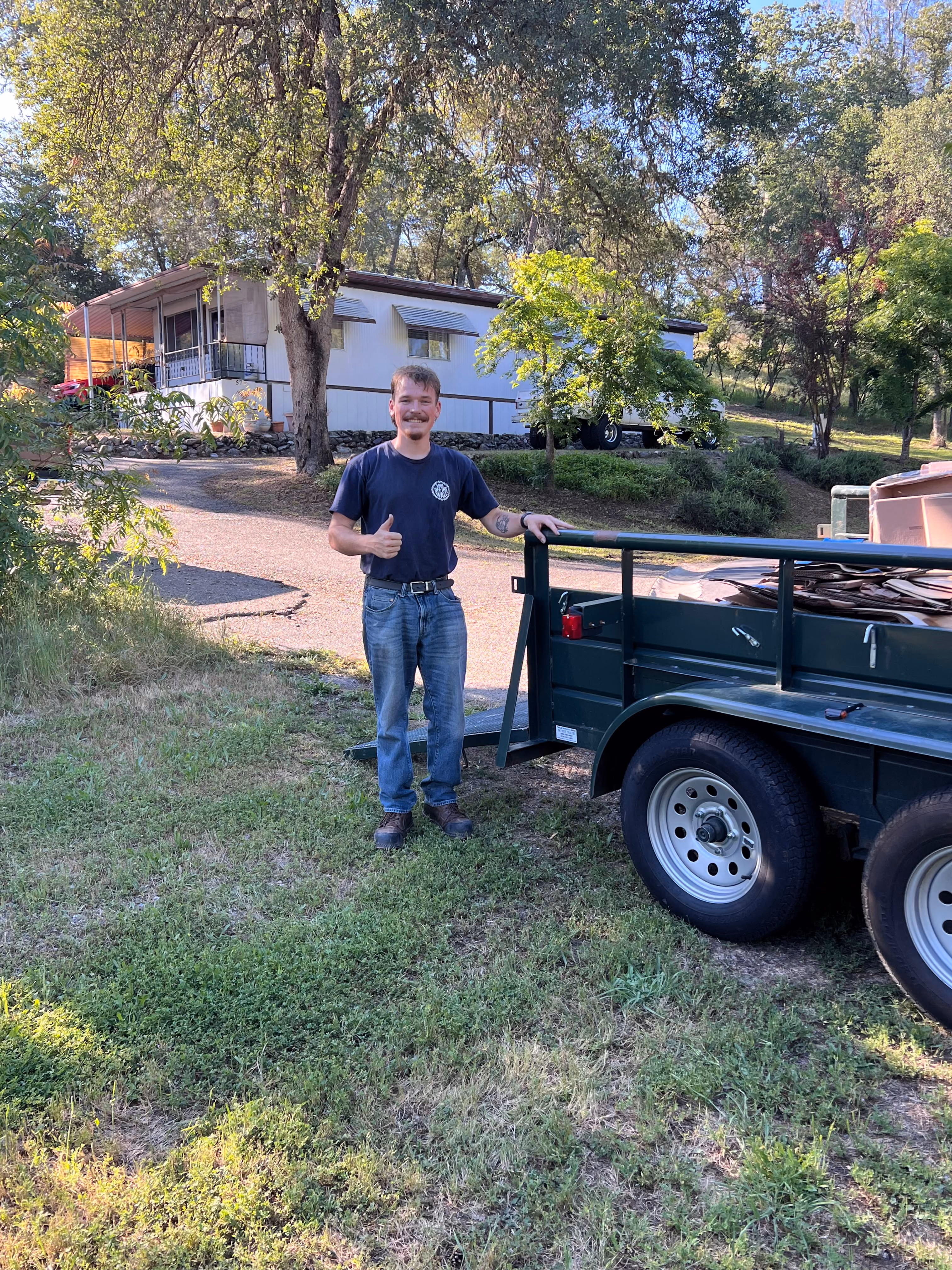 Aidan beside a utility trailer loaded with old lumber at a rural foothill property