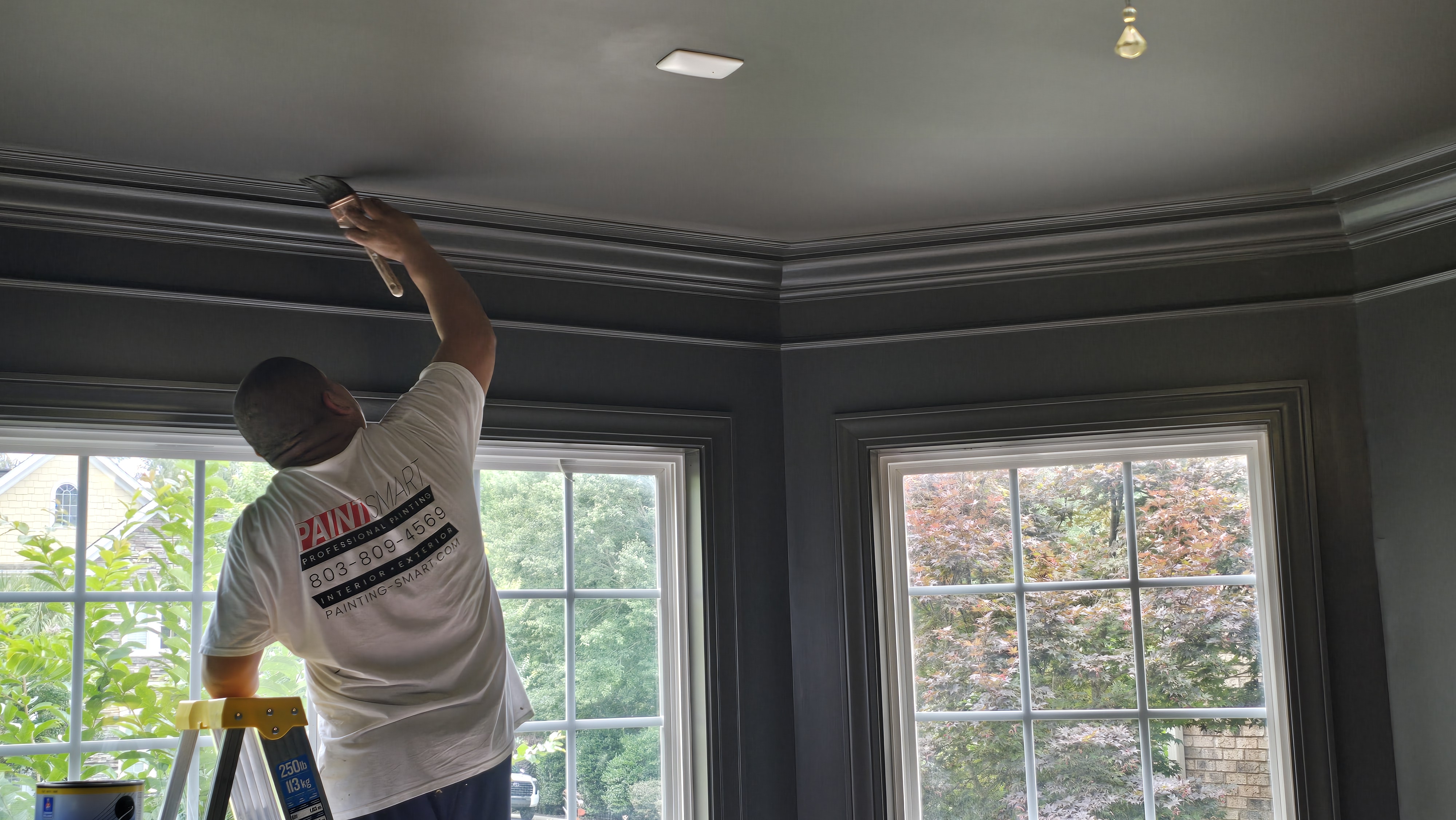 PaintSmart painter cutting in crown molding and ceiling trim against dark gray walls