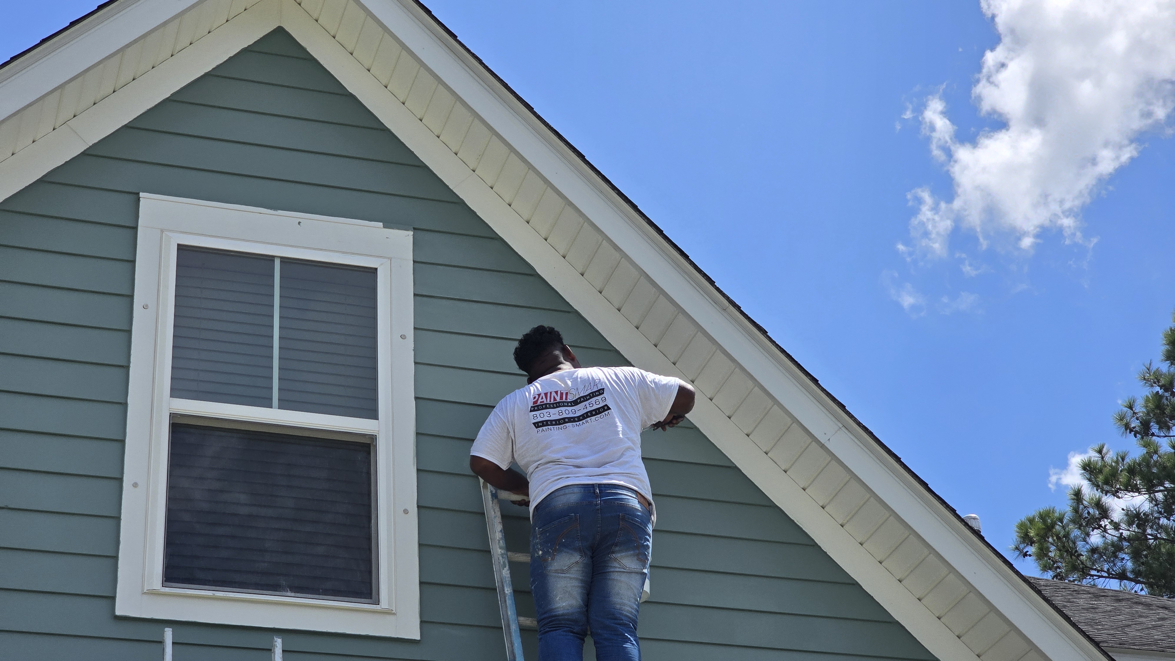 PaintSmart exterior painter on a ladder painting green siding and window trim in Goose Creek, SC