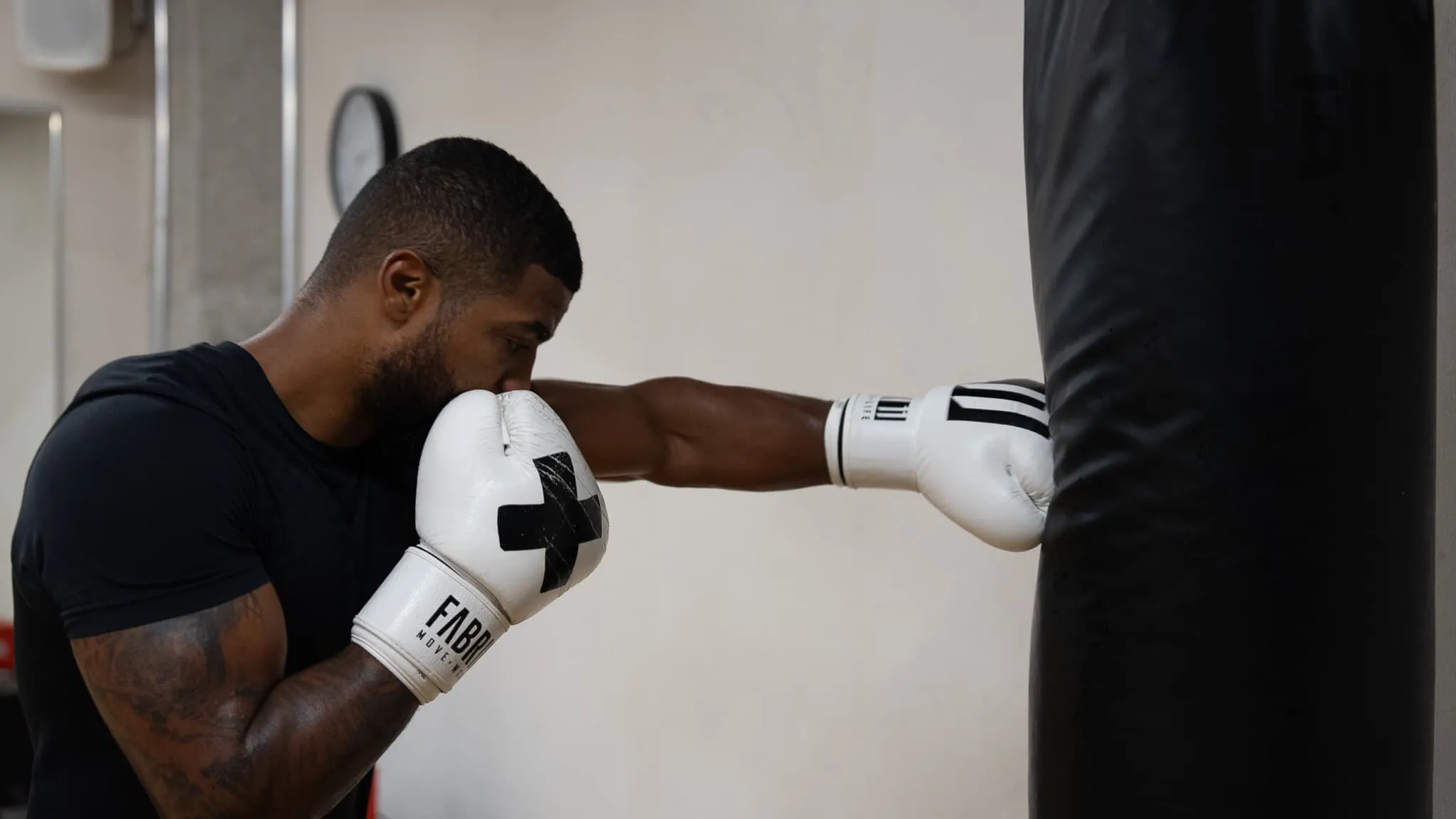 Boxer mit weissen Boxhandschuhen schlägt beim Boxtraining im ProFight Gym auf den Sandsack