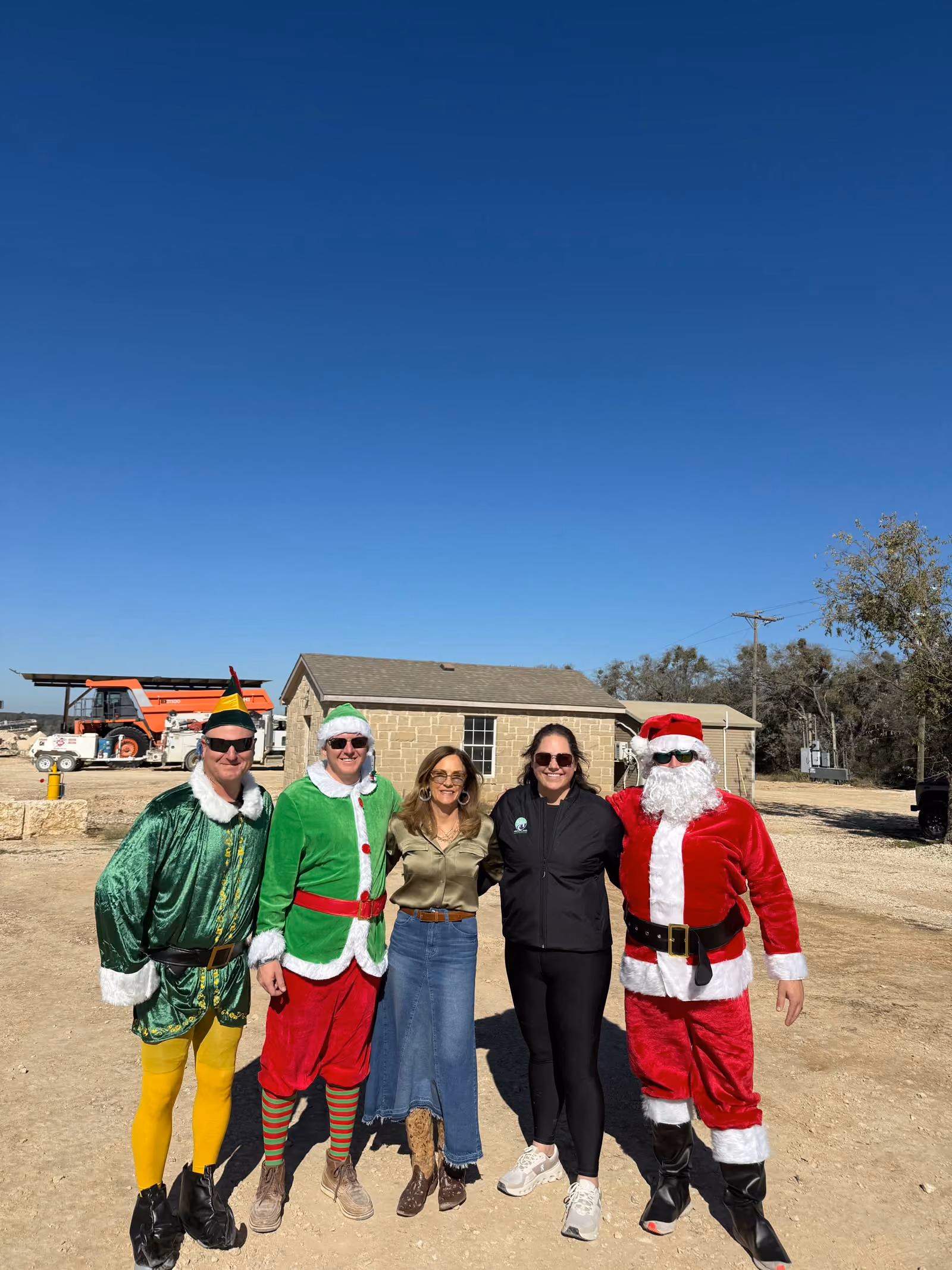 The Heartland Aggregates team in holiday costumes outside the office, with a haul truck behind them