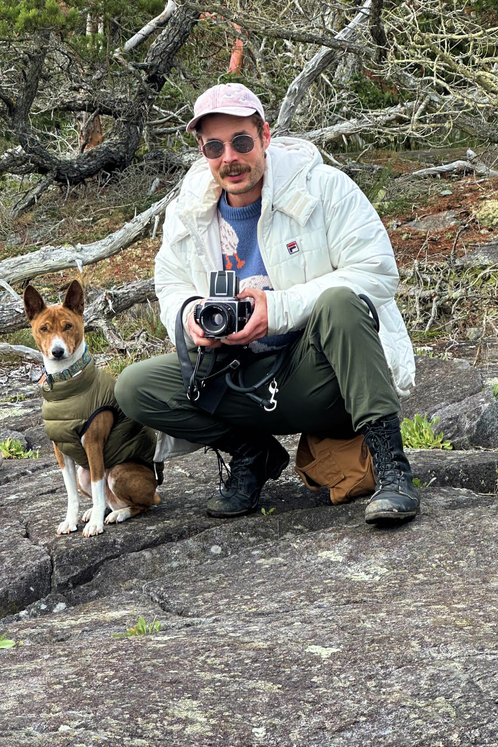 Photo of Alexander and his dog Doc Holliday taking a photo using a medium format camera while perched on large gray rocks.