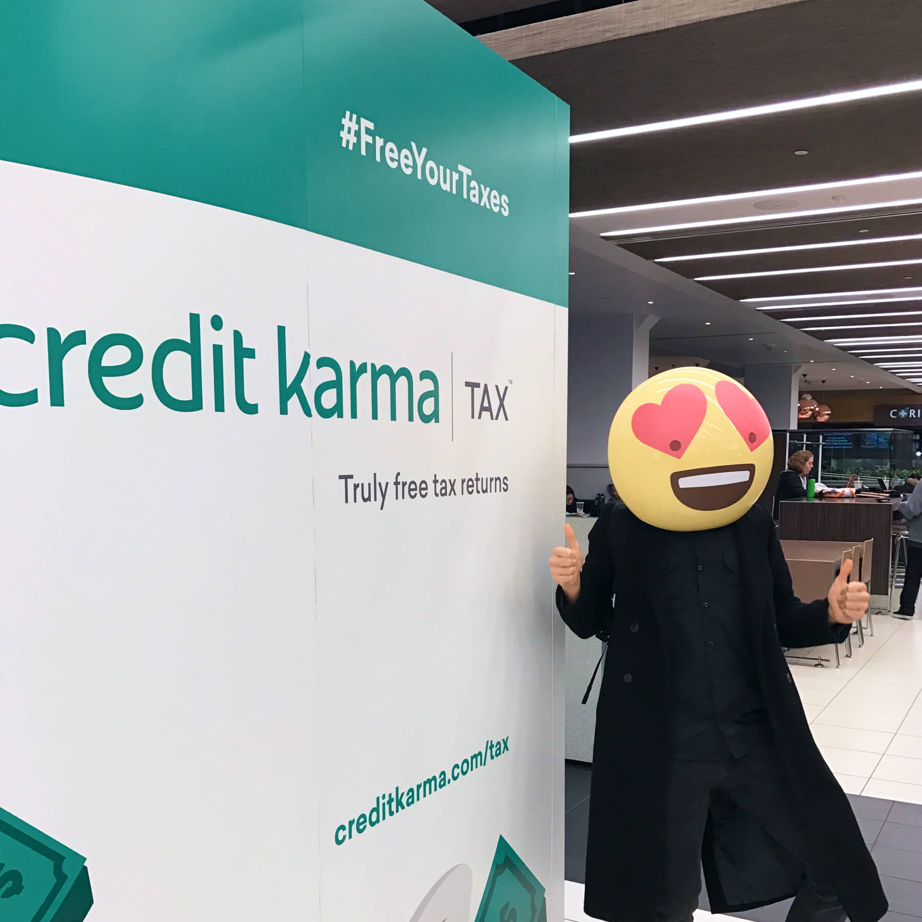 Someone in a heart-eye emoji mask in front of a Credit Karma Tax sign experiential activation