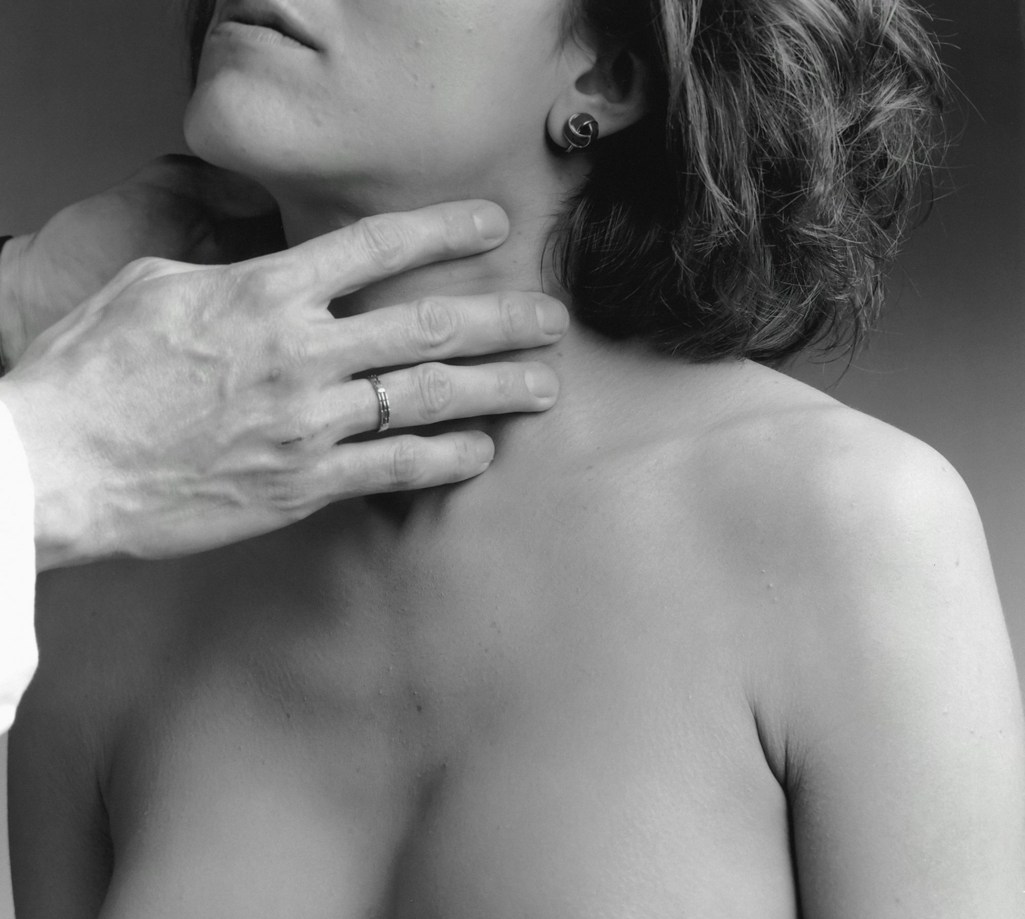 Clinician's hand gently examining the front of a woman's neck where the thyroid gland sits (posed by models)