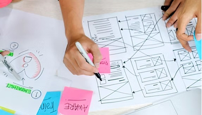 Close-up of a hand sketching a website wireframe on paper, surrounded by sticky notes.