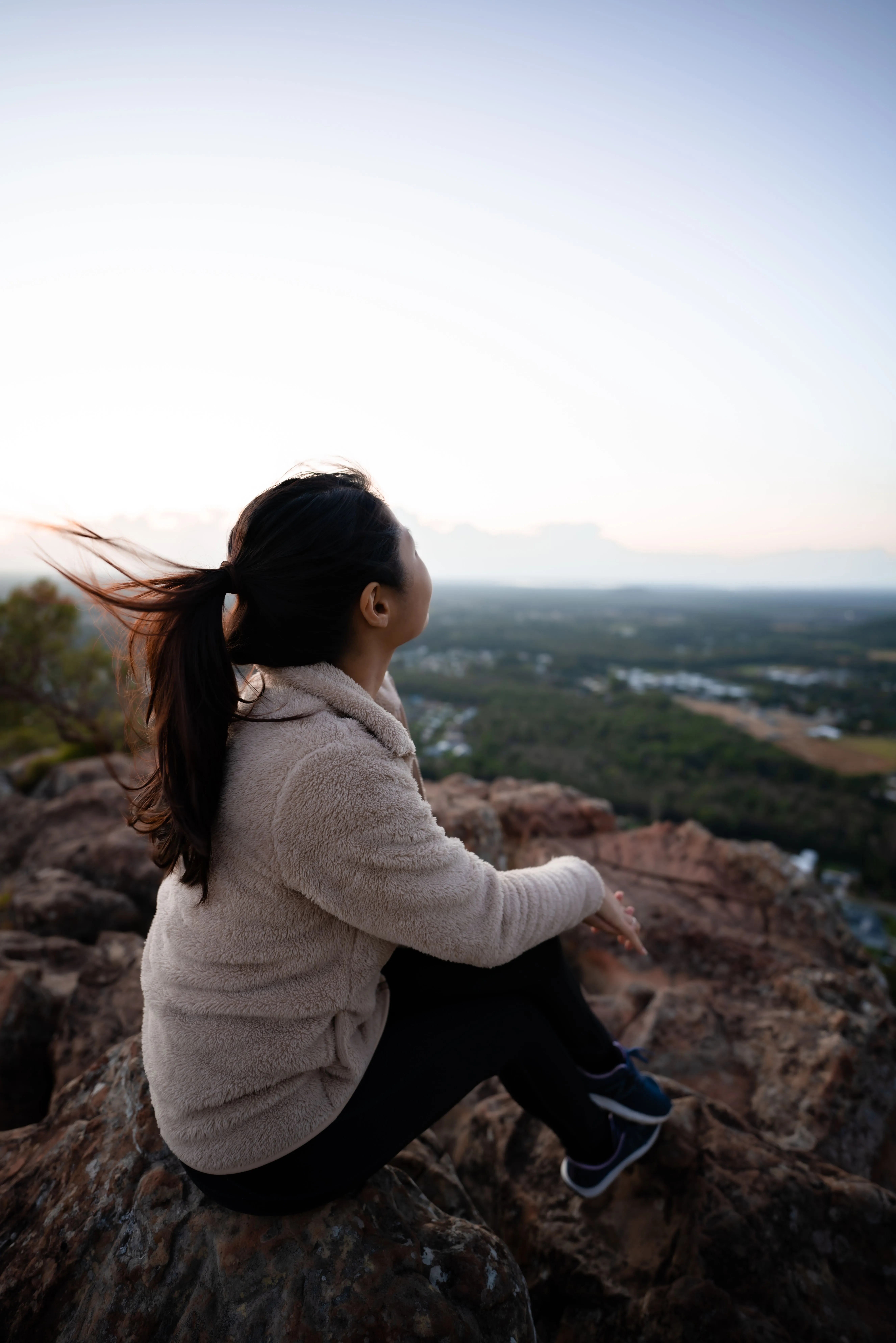 A woman sitting on a rock at dusk, looking out over the valley below