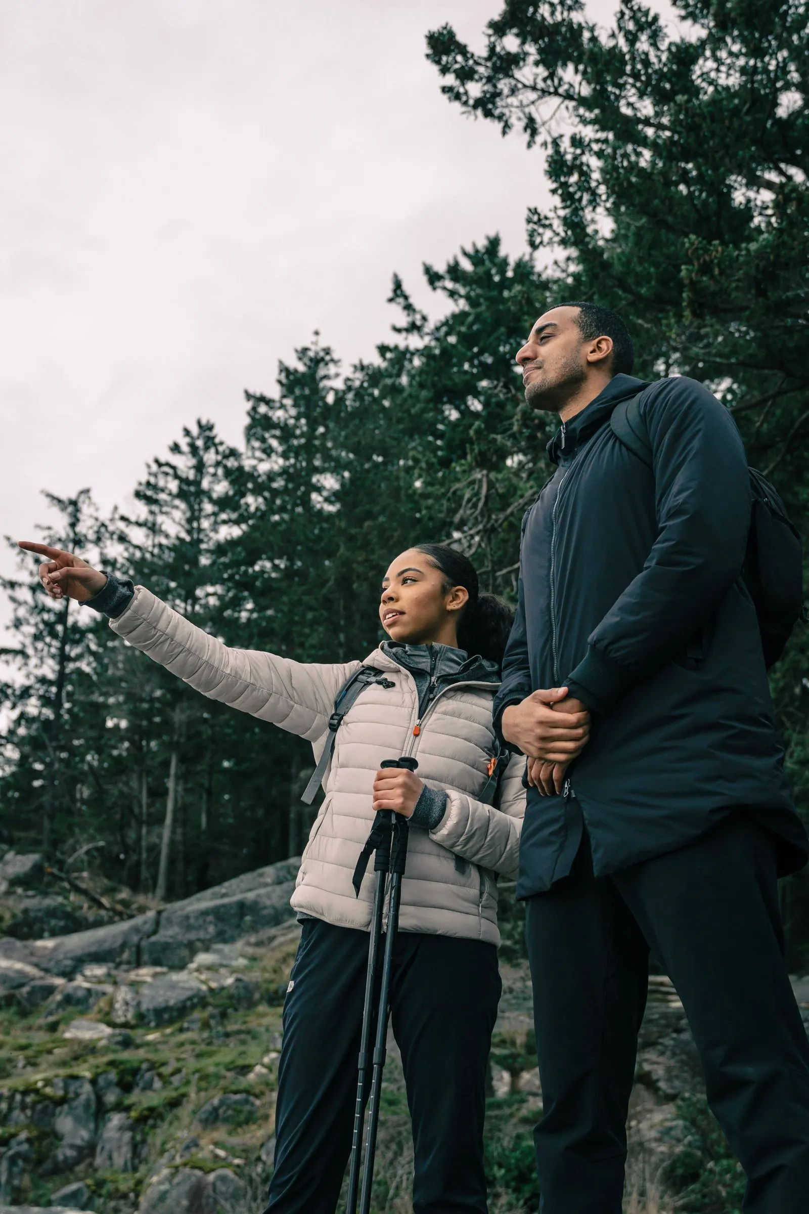 Two people standing side by side on a rocky outcrop, one pointing toward the horizon