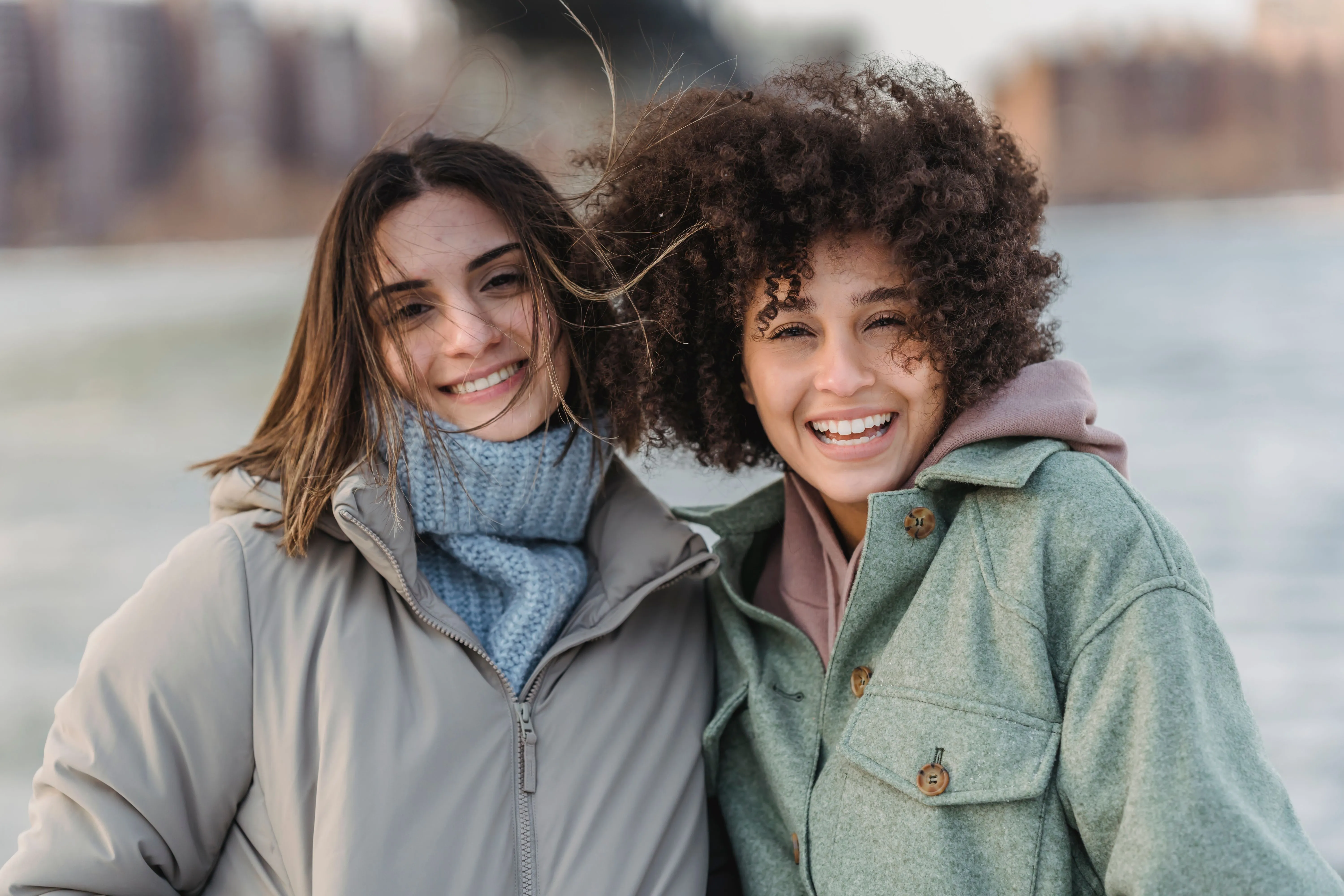 Two friends smiling by the water on a windy day