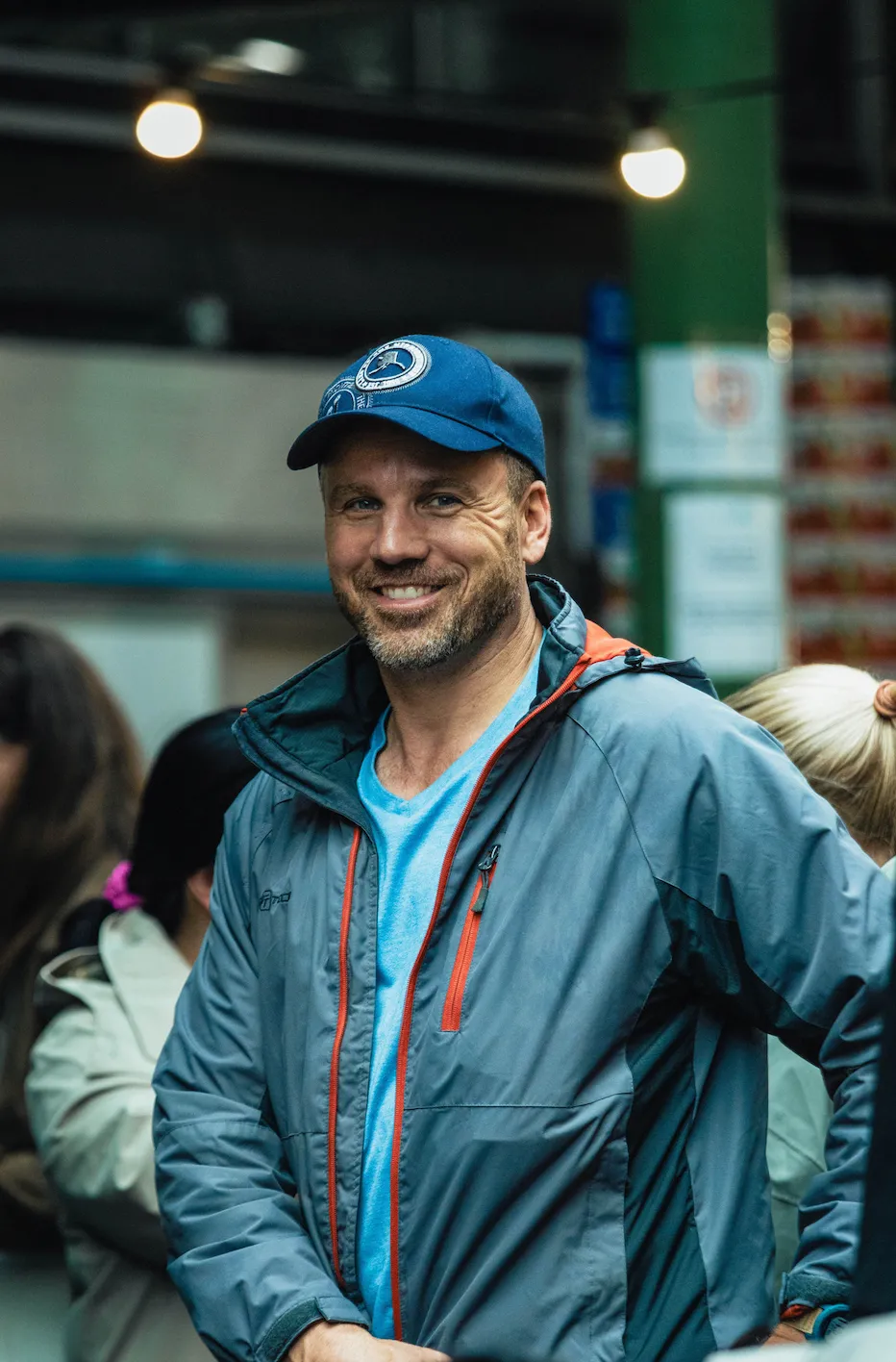 A man in a ball cap smiling in a busy market