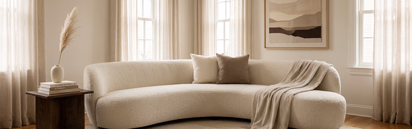 Serene neutral living room with a curved cream sofa, sheer linen drapery and soft natural light