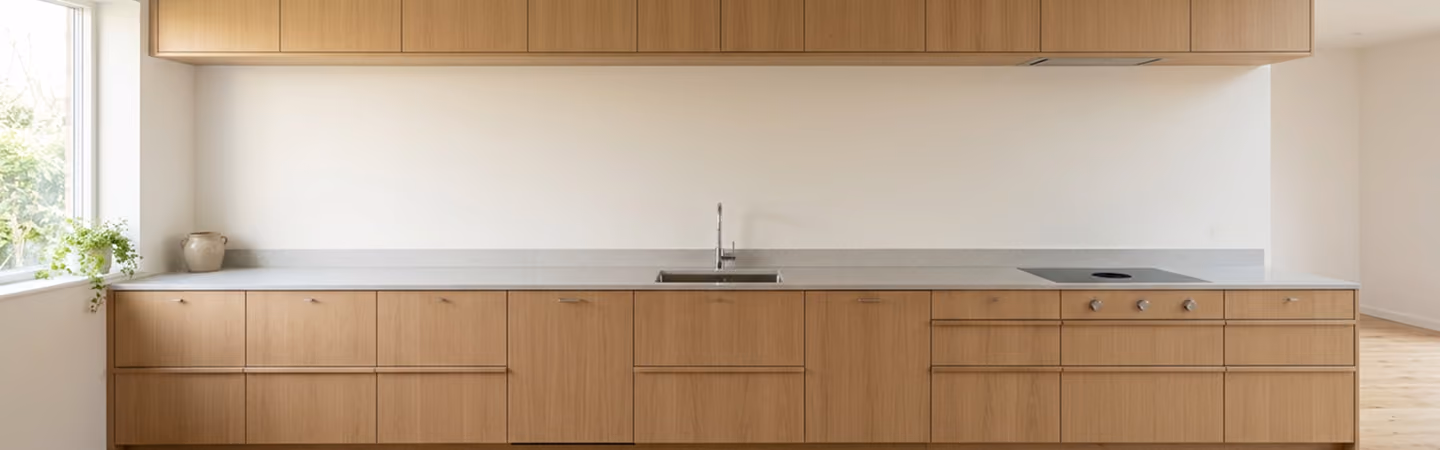 Minimal kitchen wall of flat-panel oak cabinetry with a white stone countertop