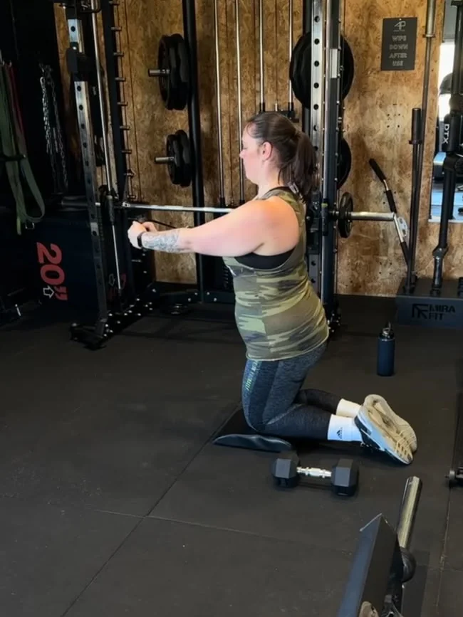 Stacey kneeling at the cable machine mid-session during her coaching
