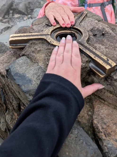 Two hands on the summit marker at the top of the mountain Stacey hiked