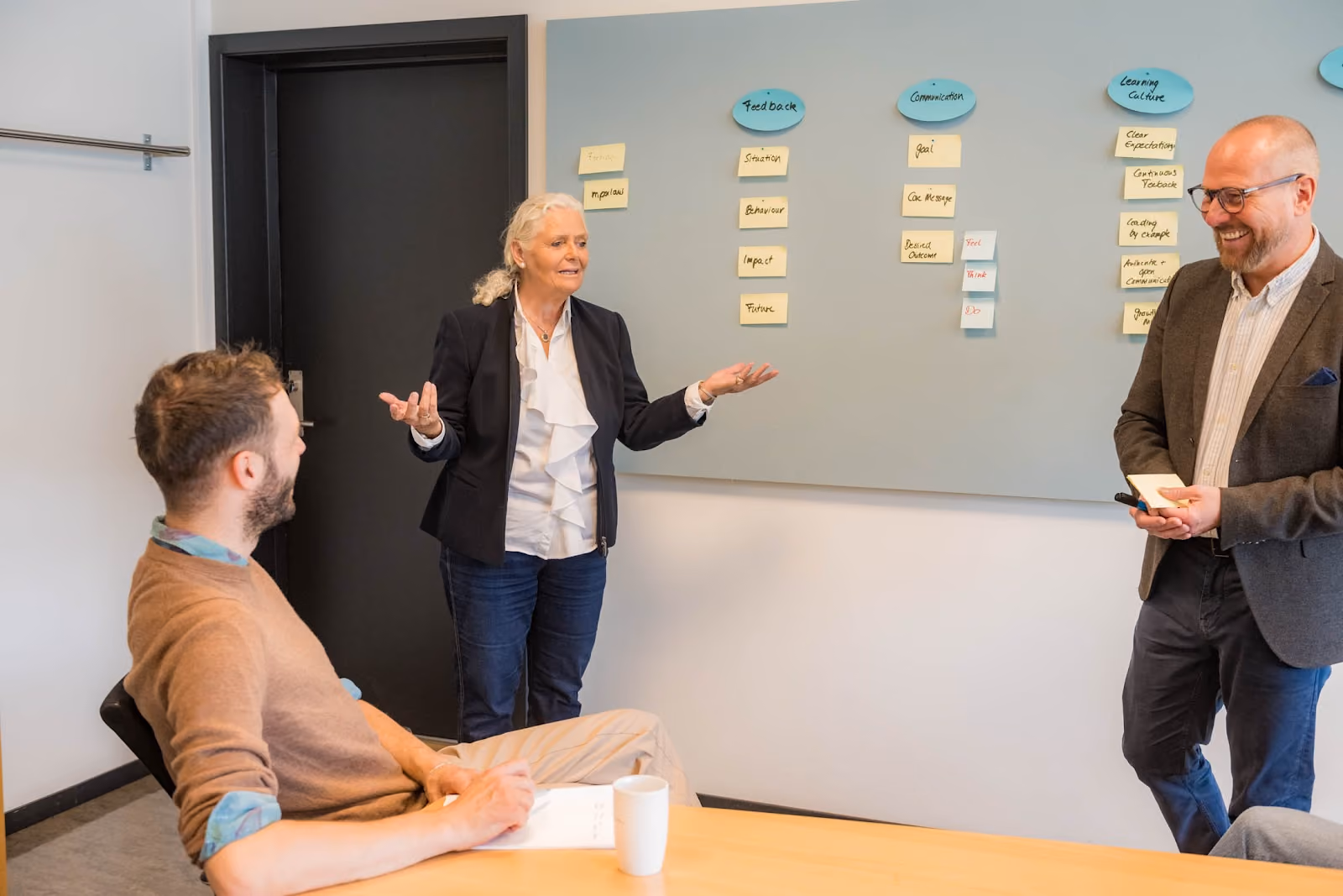 Facilitator leading a workshop in front of a board of sticky notes with participants