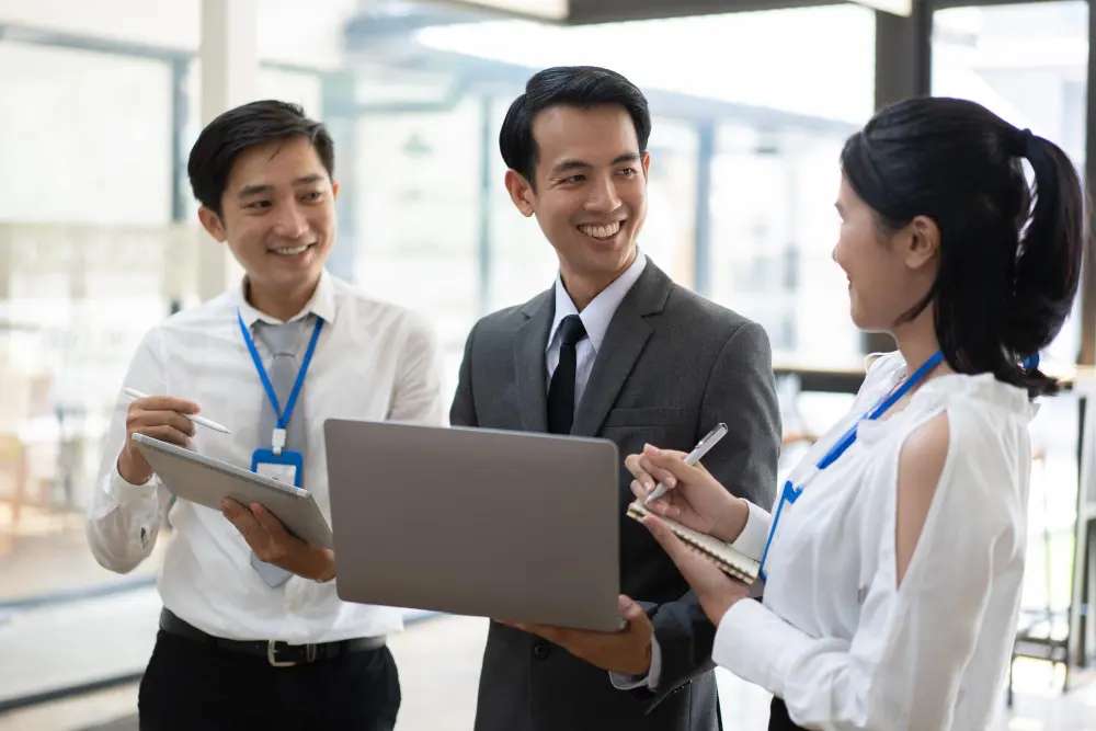 Three colleagues with a laptop and tablet talking and smiling in an office