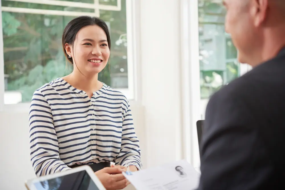 A woman smiles as she answers questions across a table in a one to one practice conversation