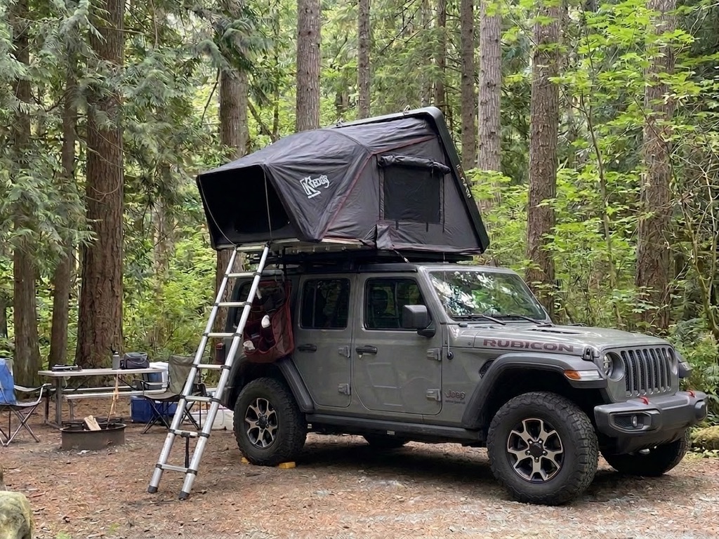 Jeep Wrangler set up for forest camping with rooftop tent among evergreen trees