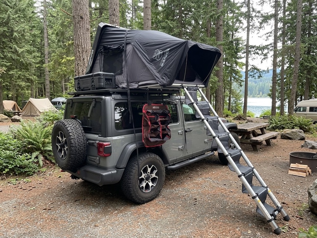 Side view of slate Jeep Wrangler with rooftop tent at a wooded campsite