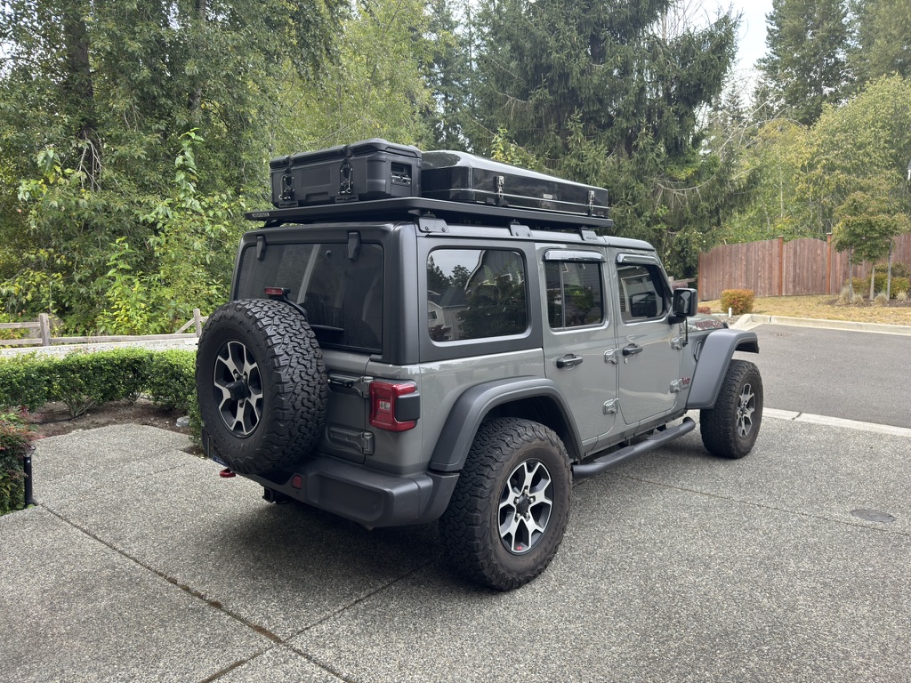 Grey Jeep Wrangler with roof platform, cases, and overland gear ready for the trail