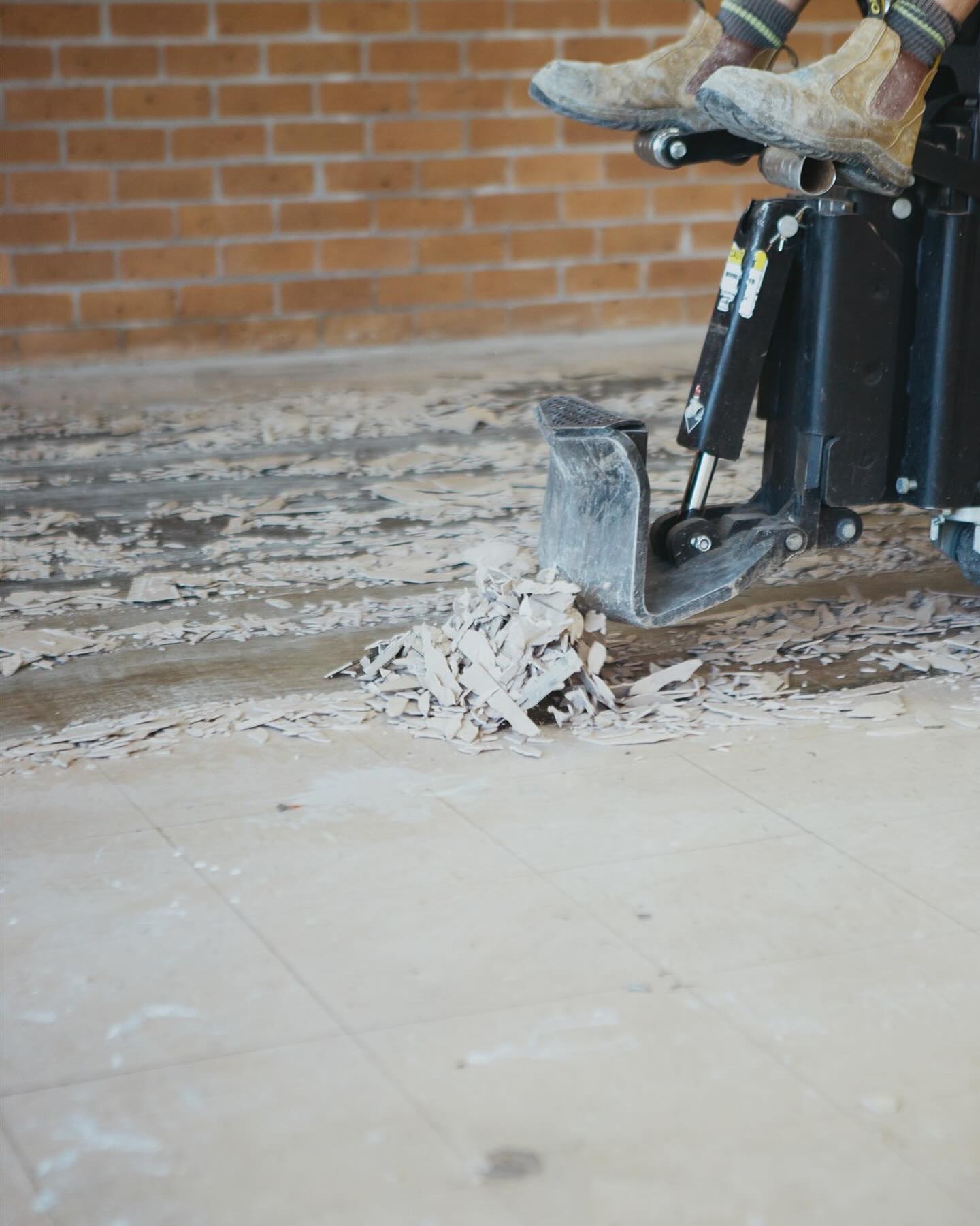 Scraper blade lifting ceramic floor tiles and bedding off the concrete slab