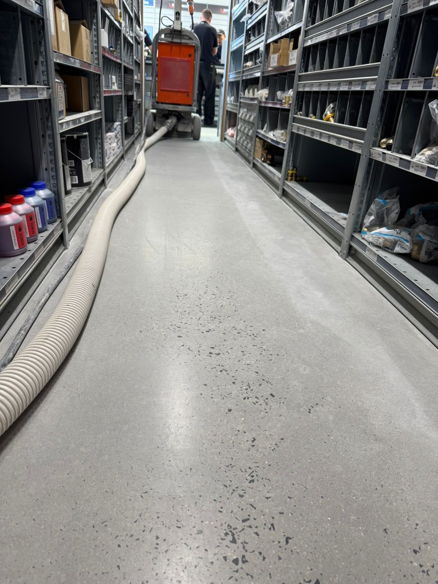 Blast Prep Grind operator running a dust-extracted floor grinder along a stocked aisle in a trade store, exposing aggregate in the concrete