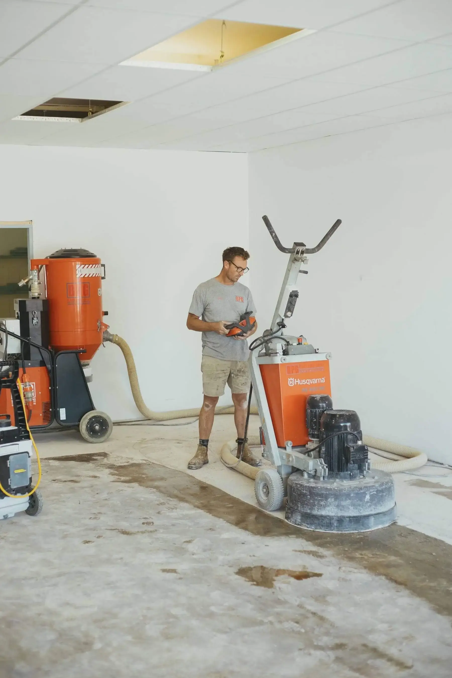 Operator running a floor grinder with dust extractors in a stripped interior