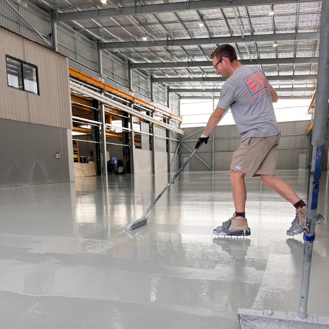 Applicator spreading epoxy coating across a warehouse floor with a squeegee