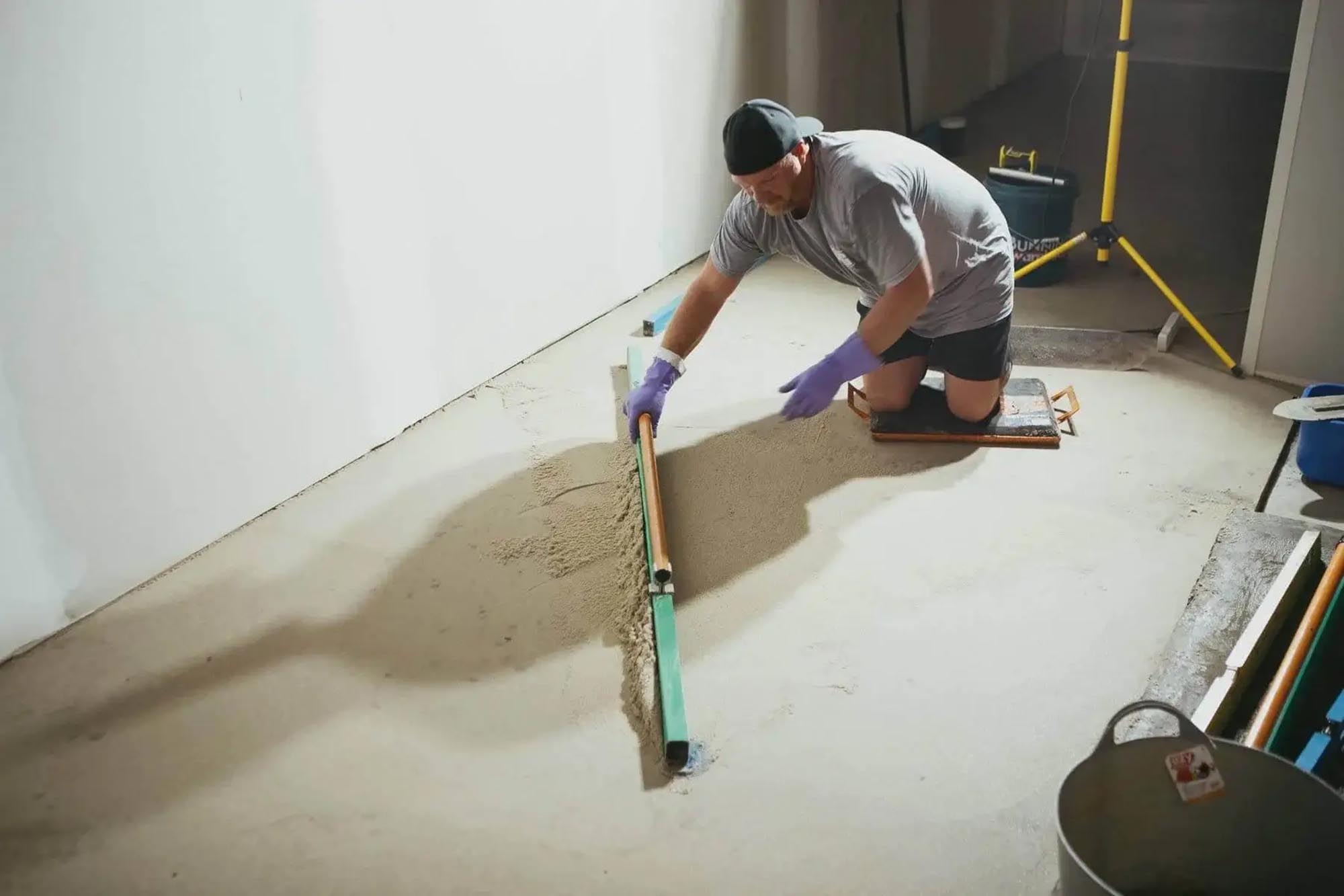 Worker kneeling to spread material across a prepared concrete floor