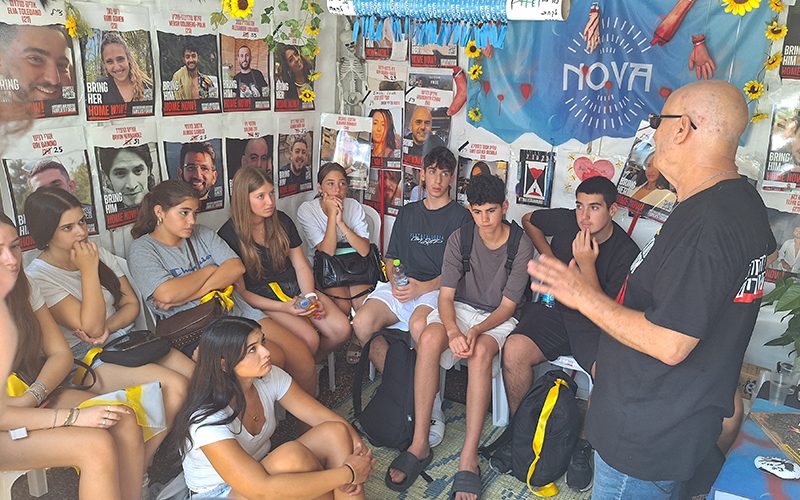 Young participants listen to a speaker in a room lined with posters and tributes.