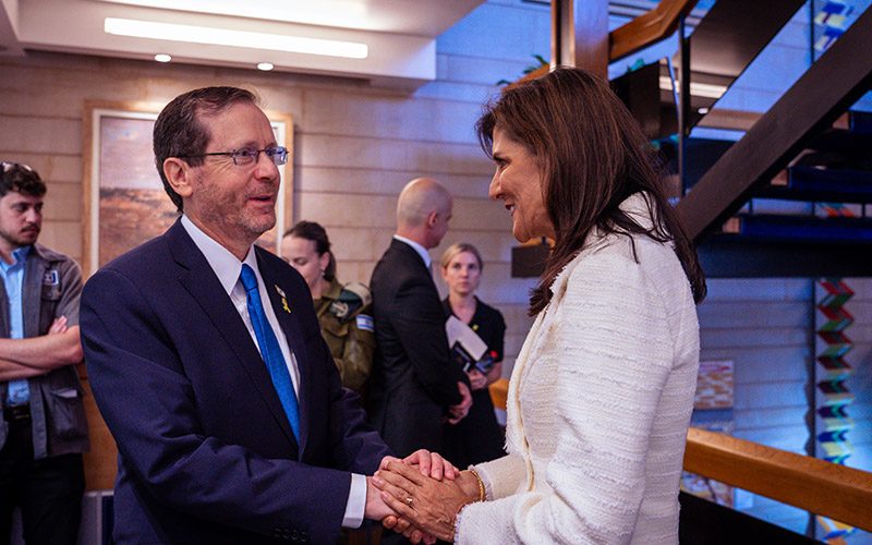 Two people greet one another and shake hands during an indoor gathering.