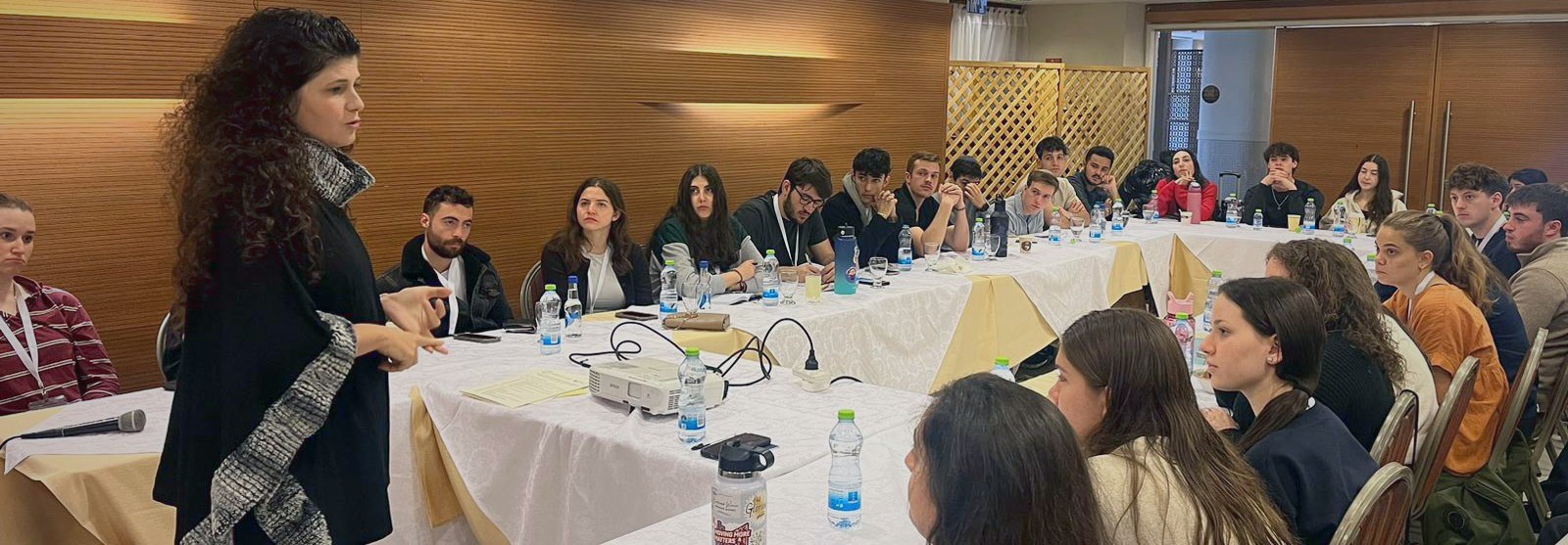 A speaker leads a seminar with student leaders around a conference table.