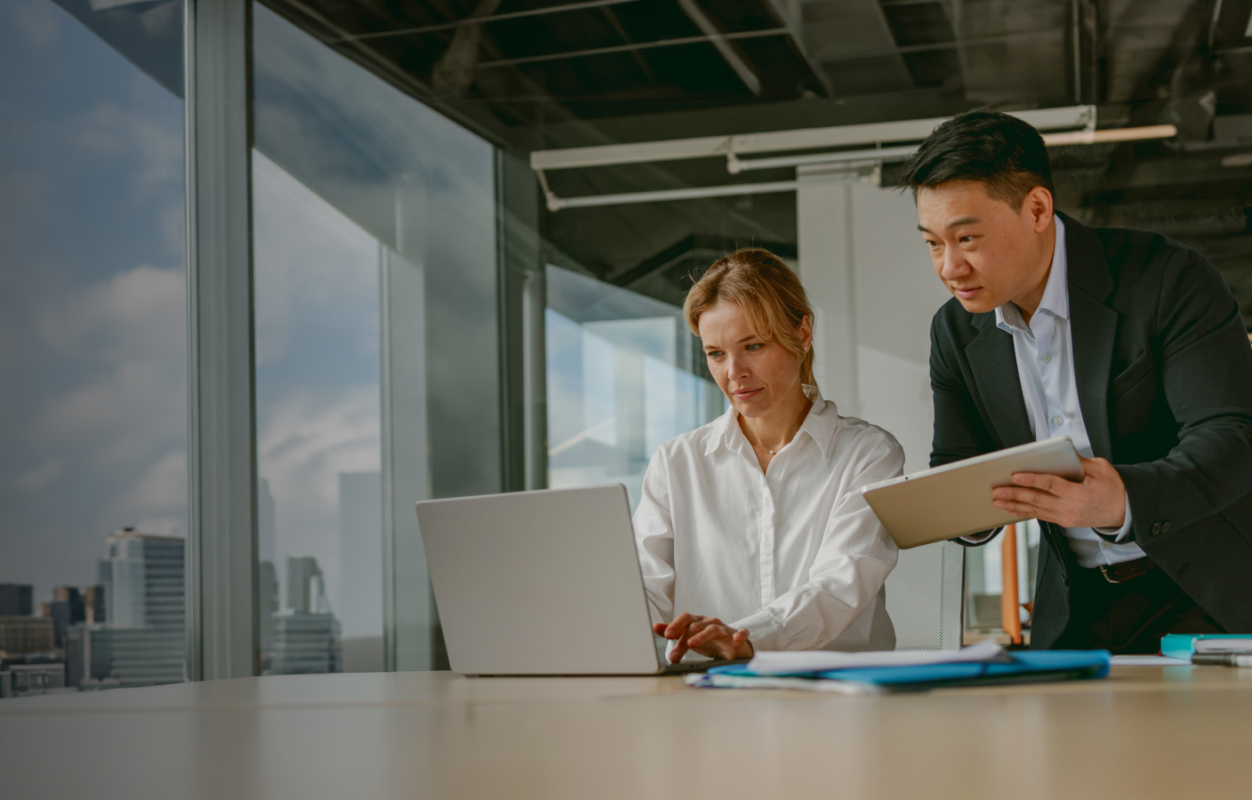 Two business professionals reviewing information on a laptop and tablet in an office.