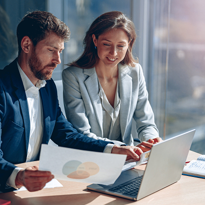 Business professionals reviewing documents and a laptop at a meeting table.