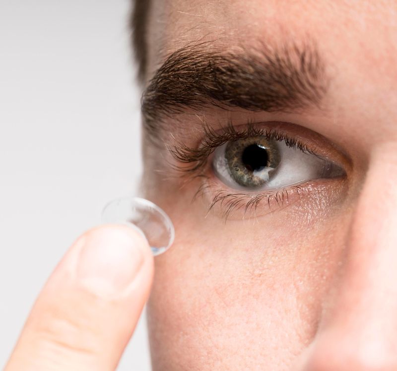 Close-up of a person holding a clear contact lens on their fingertip near their eye, preparing to put it in.