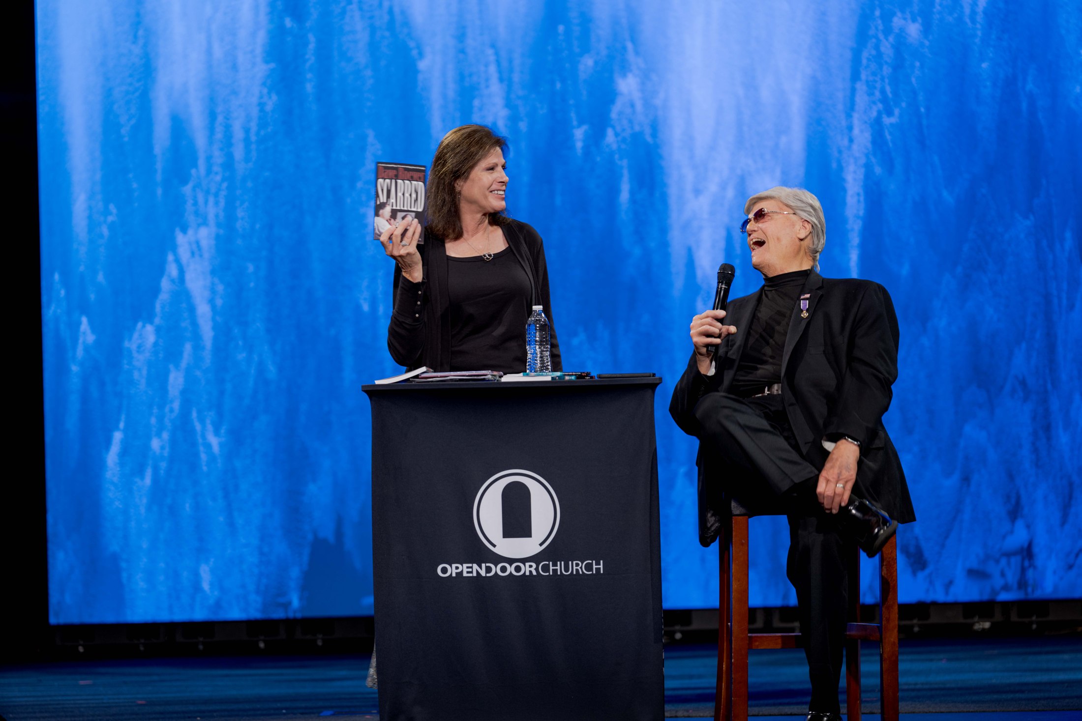 Two church leaders speaking on stage against a blue screen
