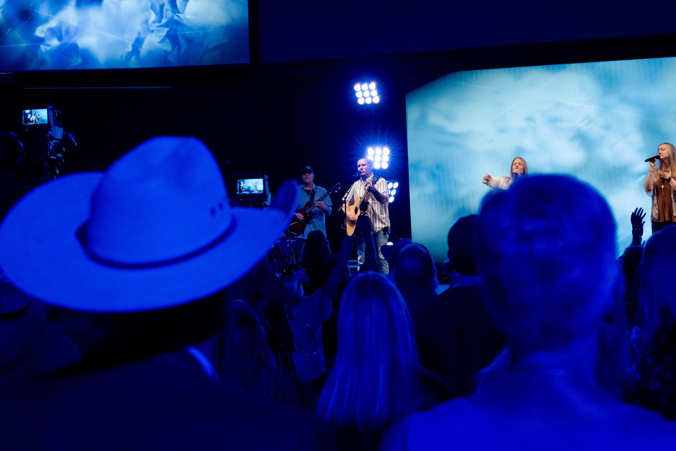 A blue-lit stage viewed between audience silhouettes