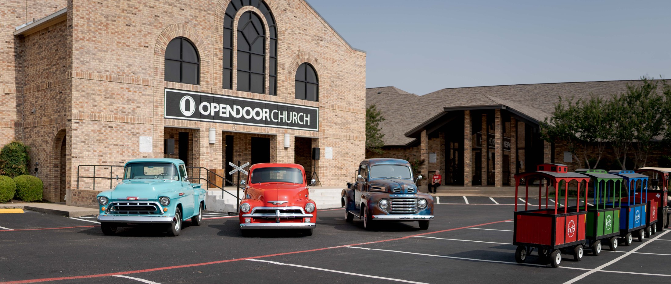 OpenDoor Church exterior with vintage cars and a colorful visitor tram