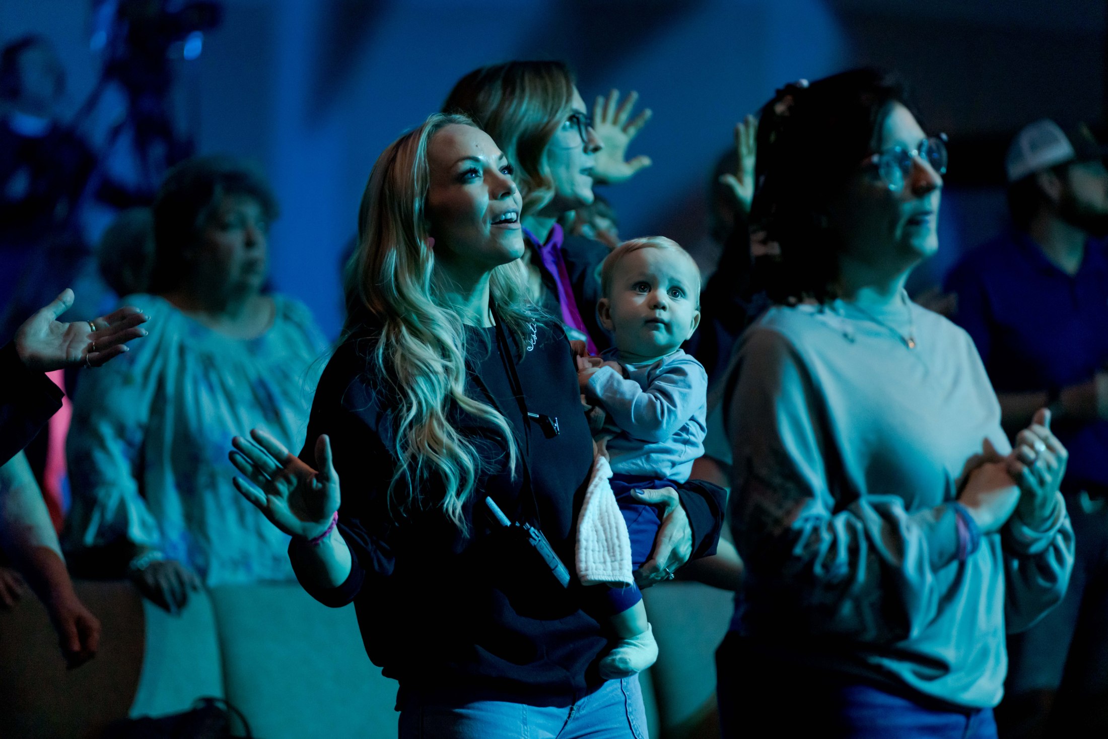 A mother holding her baby among worshippers in blue and teal light