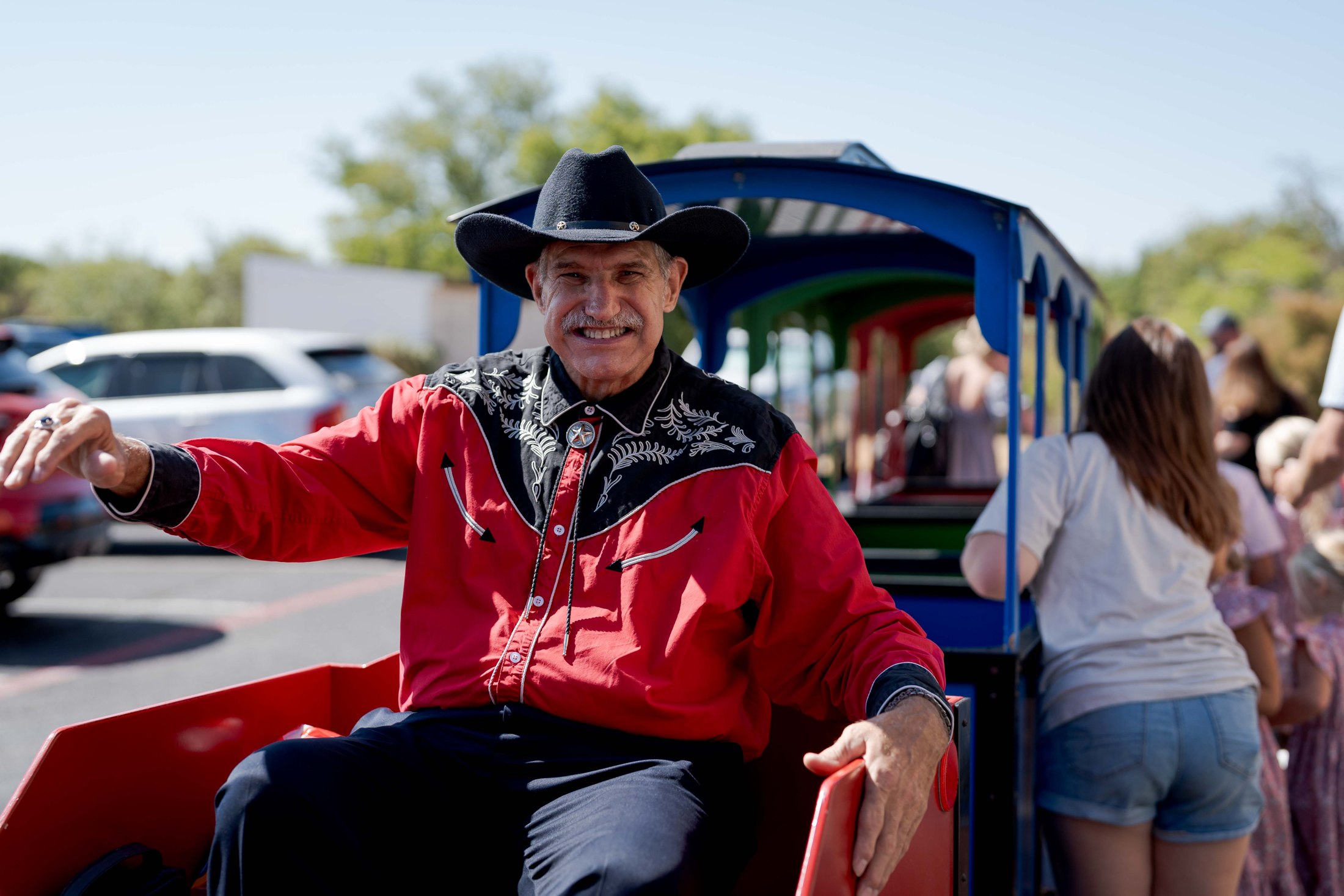 A smiling man in a red shirt beside a colorful visitor tram