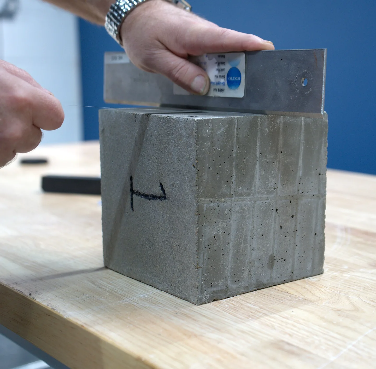 Technician checking a concrete cube with a steel straightedge on a laboratory bench