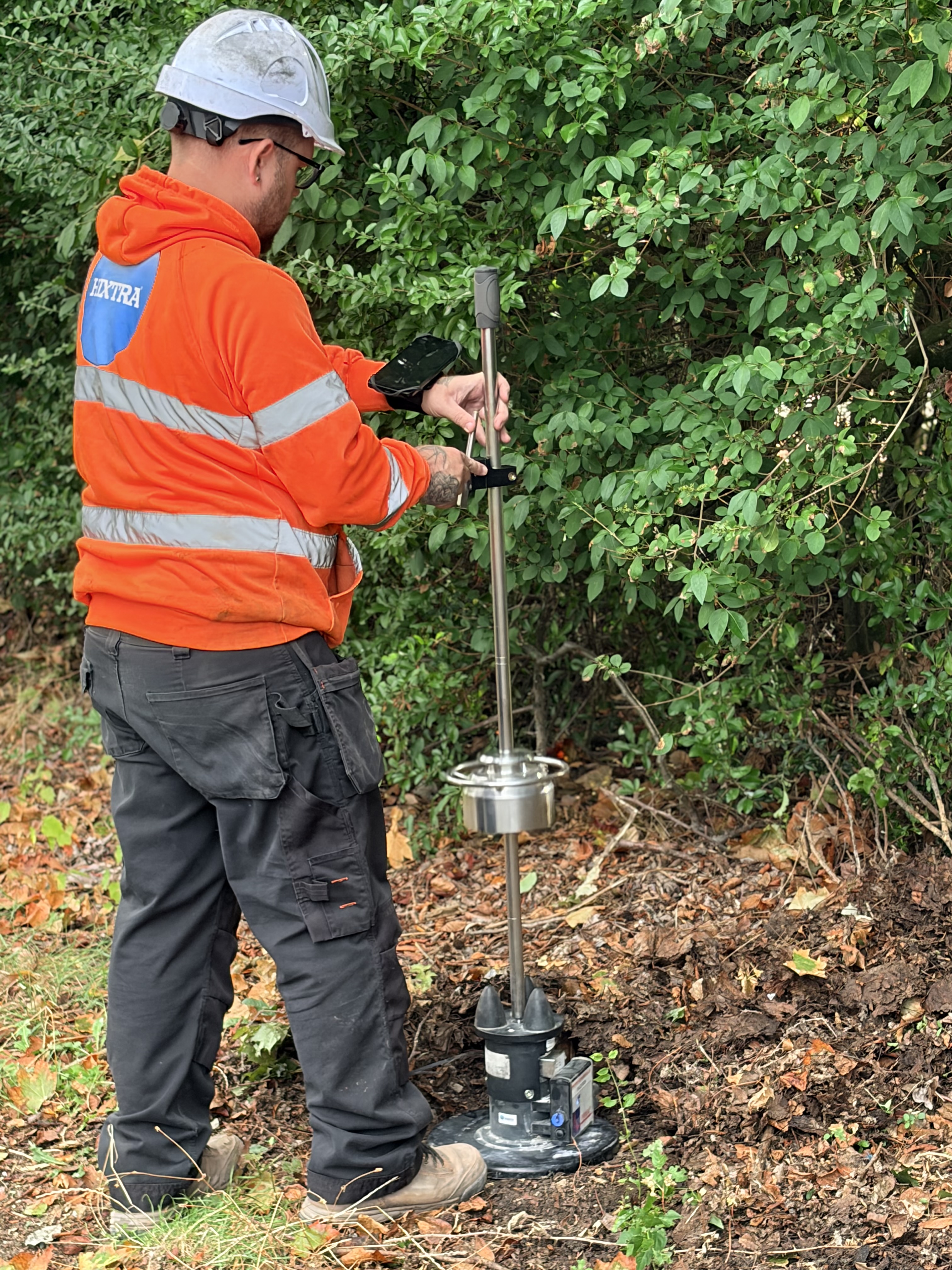 Hixtra technician carrying out a light weight deflectometer test beside a hedge