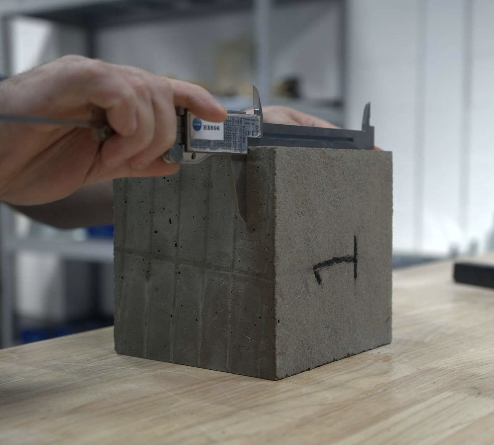 Hand measuring a concrete test cube with a vernier caliper