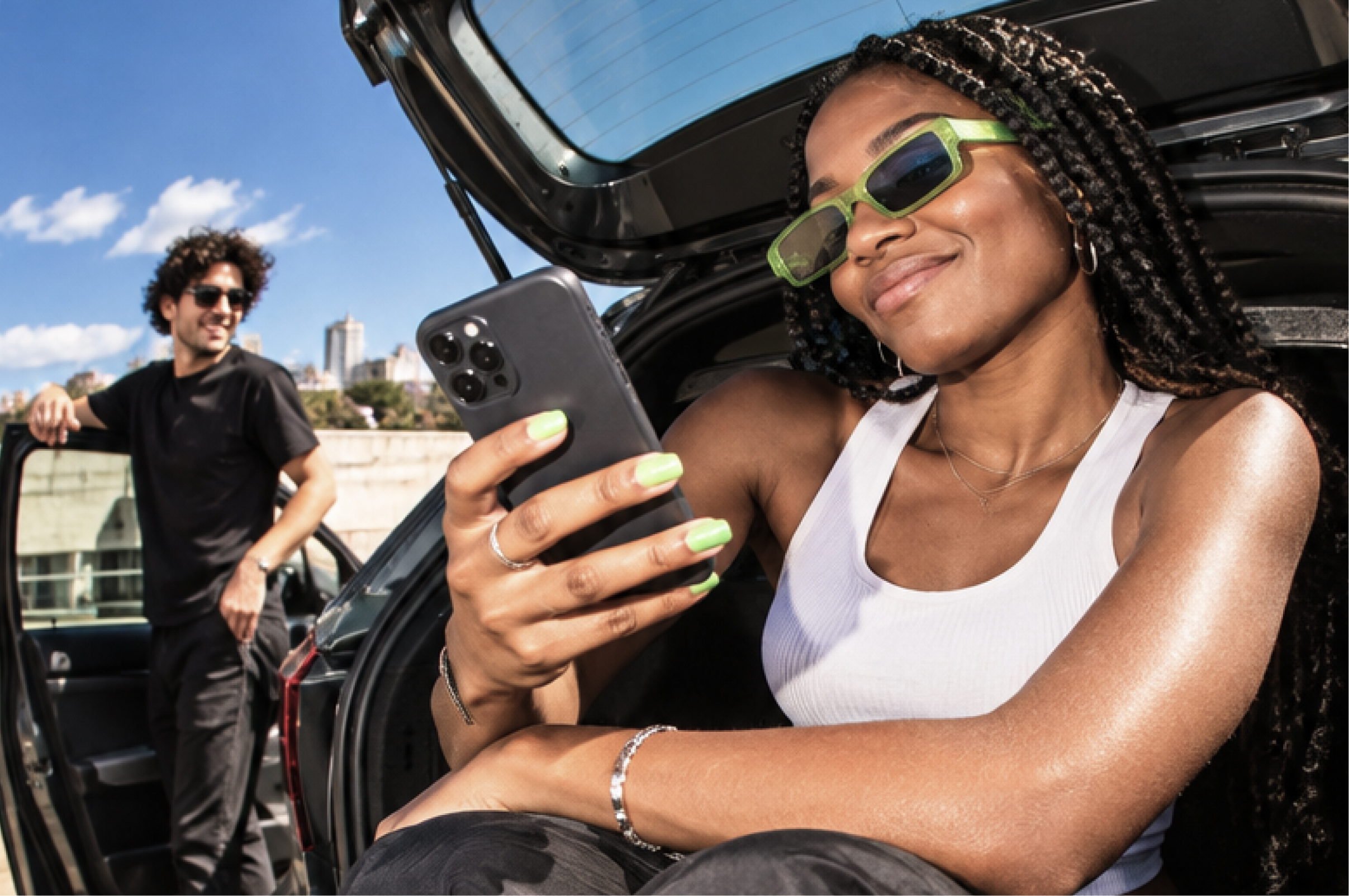 Mulher sorridente com telemóvel sentada na bagageira de um carro